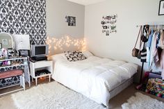 a white bed sitting in a bedroom next to a wall with pictures and lights on it