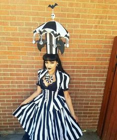 a woman dressed in black and white is standing next to a brick wall