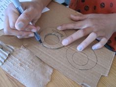 two hands are holding scissors and drawing on cardboard with circles in the middle, while another person is sitting at a table behind them