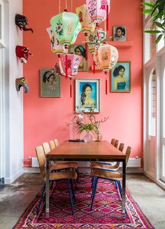 a dining room with pink walls and pictures hanging on the wall above the wooden table