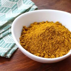 a white bowl filled with yellow powder sitting on top of a wooden table next to a napkin