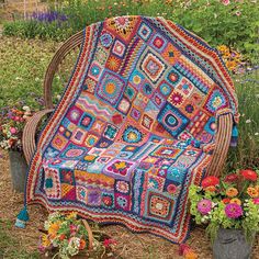 a colorful crocheted blanket sitting on top of a wooden bench next to flowers