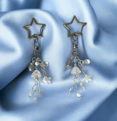 two star shaped earrings with dangling beads on a blue satin background, one is silver and the other is white