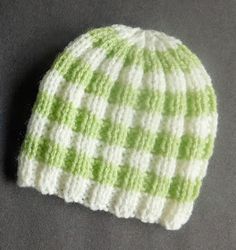 a green and white knitted beanie sitting on top of a gray table next to a cell phone