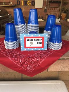 blue cups and plates are on a red table cloth in front of a stove top