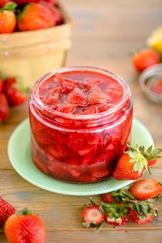 a glass jar filled with strawberry jam on top of a green plate next to sliced strawberries