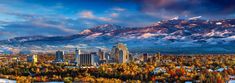 a city with mountains in the background and snow covered trees on the ground, under a cloudy sky