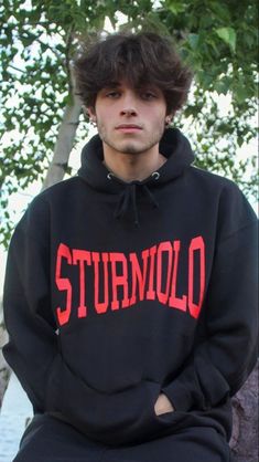 a young man sitting on top of a tree wearing a black hoodie