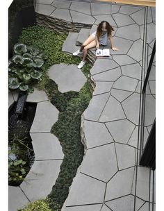 a woman sitting on a bench next to a small pond with plants growing in it