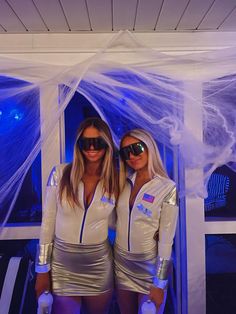 two women dressed up in costumes posing for a photo with white net covering the windows behind them