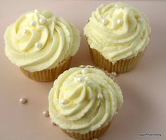 three yellow cupcakes with white frosting and pearls on the top are sitting next to each other