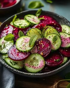 a bowl filled with cucumbers, beets and mints on top of a wooden table