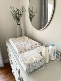 a white dresser topped with a baby's crib next to a round mirror