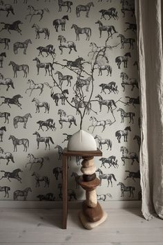 the wallpaper has horses on it and is next to a table with a lamp