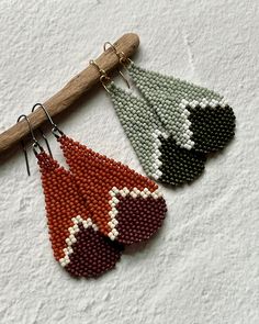 two pairs of beaded earrings hanging from a wooden stick on top of a white surface