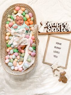 a baby in a basket surrounded by easter eggs and other decorations on a white sheet