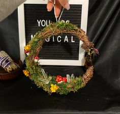 a wreath with mushrooms and flowers is being held up by someone's hand over a sign that says you are musical