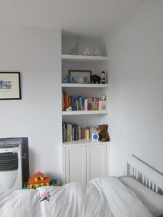 a white bed sitting in a bedroom next to a book shelf with books on it