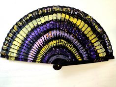 a colorful fan sitting on top of a white wall next to a black object with yellow and purple designs