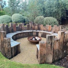 an outdoor fire pit made out of logs in the middle of a garden with trees and bushes around it