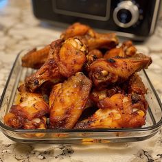 some chicken wings are in a glass dish on a counter top next to a digital camera