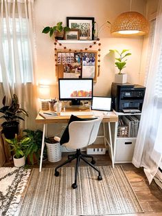 a desk with a computer on top of it next to a window and potted plants