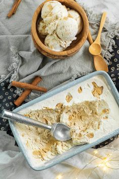 two scoops of ice cream sit in a bowl next to cinnamon sticks and spoons