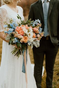 a bride and groom standing next to each other in the grass holding bouquets with flowers on them