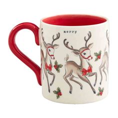 a red and white coffee mug with reindeers on it's side, decorated with holly berries