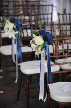 chairs with blue sashes and white flowers on them are set up for an outdoor ceremony