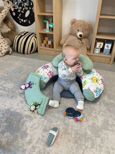 a baby is sitting on the floor with stuffed animals around him and looking at his teeth