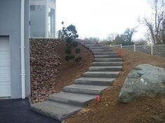 concrete steps lead up to the side of a house on a hill with rocks and trees