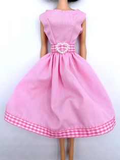 a barbie doll wearing a pink dress with white checkers on the skirt and shoes