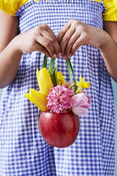 a person holding a red vase with yellow and pink flowers in it's hands