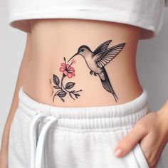 a woman's stomach with a hummingbird and flower tattoo on the side of her belly