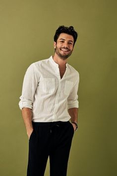 a man standing in front of a green wall wearing a white shirt and black pants