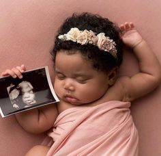 a newborn baby is sleeping on a pink blanket and holding an album with the image of a woman's face