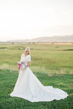 a woman in a wedding dress standing in the grass with her arms behind her back