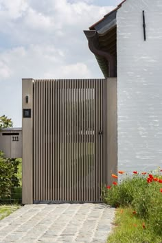 a wooden gate in front of a white building with red flowers growing on the side