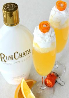 two glasses filled with orange juice next to a bottle of rum chata and an orange slice