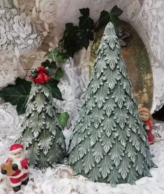 two small christmas trees sitting next to each other on a lace tablecloth covered surface