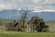 an old house in the middle of nowhere with snow capped mountains in the back ground