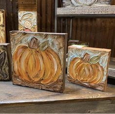 three pumpkins are painted on wood blocks in front of a wooden shelf with other items