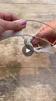 two hands are tying a rope to a piece of white string on a wooden table