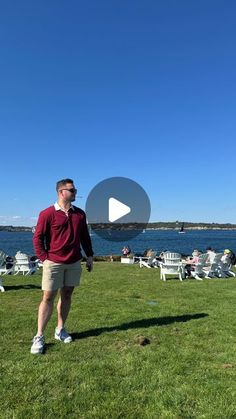 a man standing on top of a lush green field next to the ocean with people sitting in lawn chairs