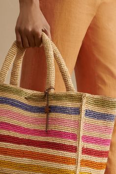 a woman holding a multicolored striped straw bag