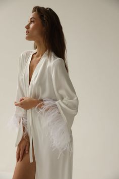 a woman in a white robe with feathers on her back and one leg bent up