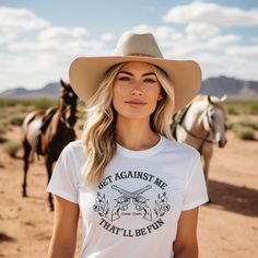 Bet Against Me That'll Be Fun Pistols t-shirt for country girls and cowgirls is a Next Level brand tee and comes in unisex cut and sizes. This graphic tee features guns and roses so to speak with its six-shooter pistols crossed in the center and pretty dainty flowers on each side. Cowgirls have a soft side until you cross them, right? This graphic tee for cowgirls is a personal favorite since my daddy called me Annie Oakley growing up. A vintage style graphic for the modern cowgirl. Looks perfec White Western T-shirt For Rodeo, White Graphic Tee For Western-themed Events, Fitted Graphic Print T-shirt For Ranch, Country Style T-shirt For Western-themed Summer Events, Pre-shrunk T-shirt For Western-themed Summer Events, Western White T-shirt For Country Events, Western Tops With Screen Print For Western-themed Events, Western Style Screen Print Tops For Western-themed Events, Western Style White T-shirt For Country Events