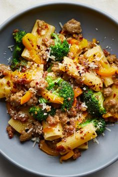 a blue plate topped with pasta and broccoli covered in meat, cheese and sauce