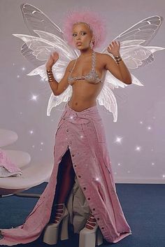 a woman dressed as a fairy with pink hair and white wings standing in front of a wall